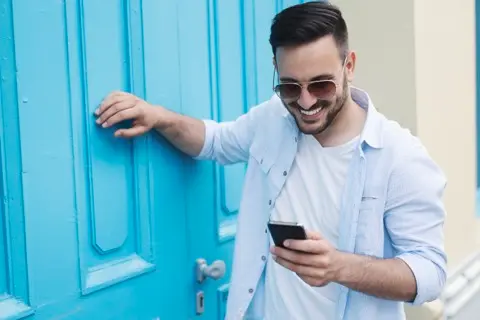 a person in front of a door looking at their phone, a bubble with an icon of a door floating towards their phone