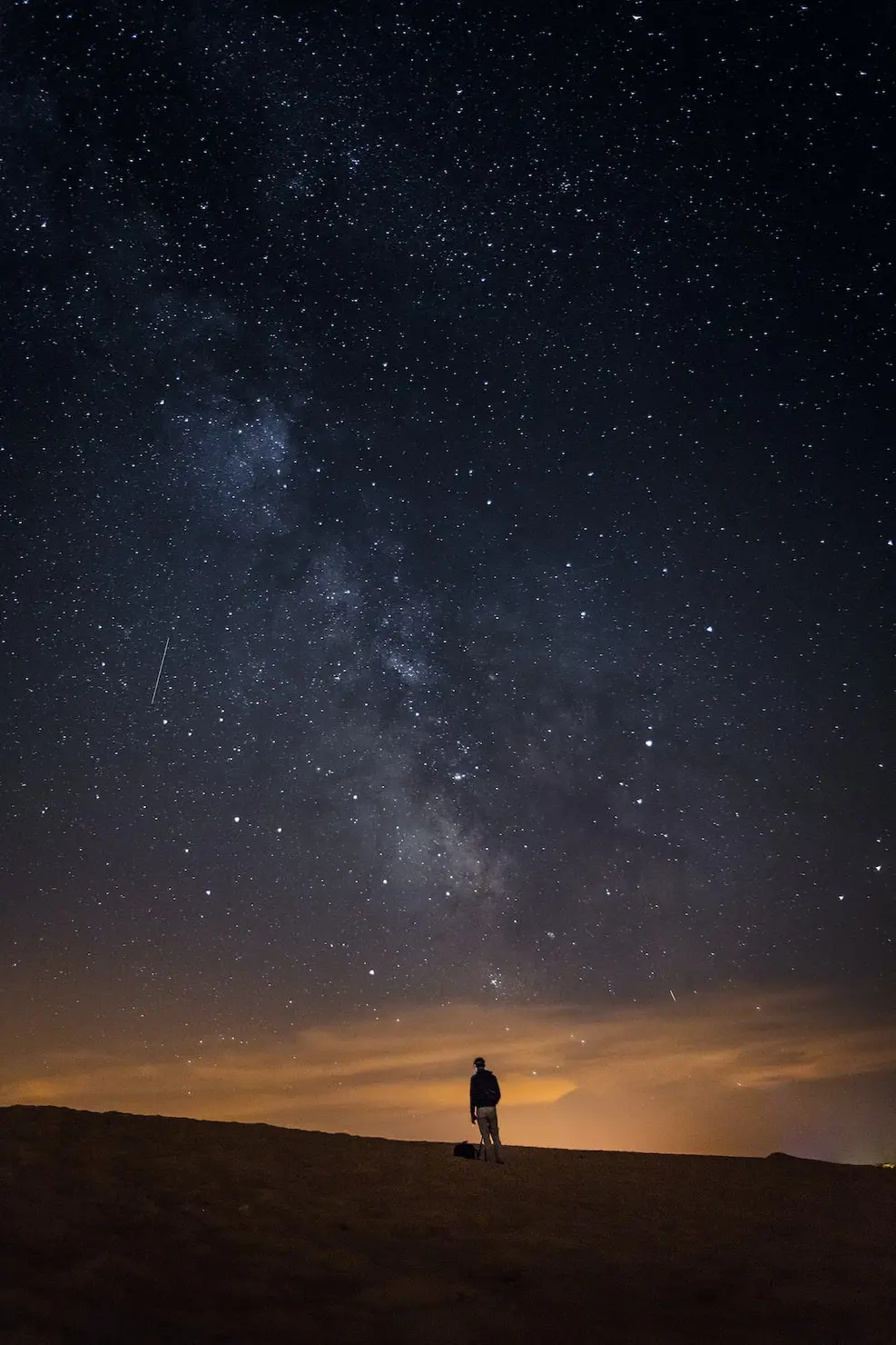 a person standing on top of a hill, looking at the night sky with a fallin star